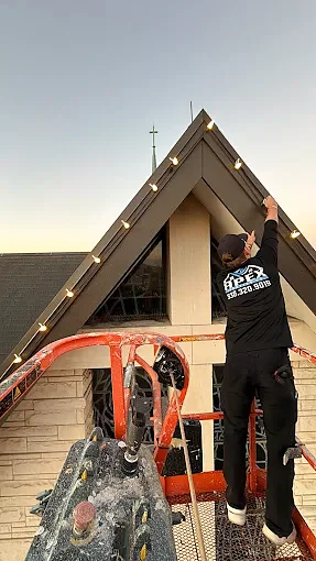 Installer on a lift attaching Christmas lights along a steep roof peak