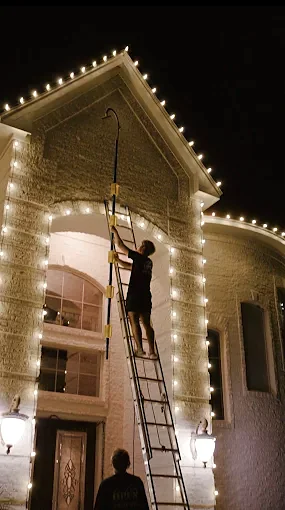 Crew member on a ladder installing roofline Christmas lights on a two-story entry
